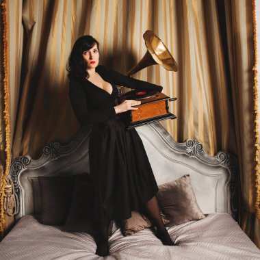 Gramofon iç stüdyo ile yatakta duran siyah seksi elbise genç güzel kadın model portresi.