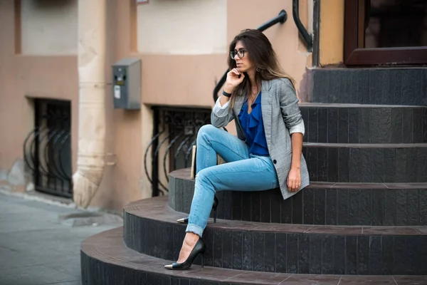 Modelo de moda en la calle. Hermosa mujer sexy en ropa de otoño de moda con estilo sentado en las escaleras — Foto de Stock