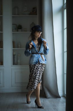 İç stüdyoda leopar elbise ayakta genç güzel kadın model moda portresi.