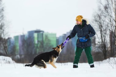 Kışın Parkta Bir Alman çoban köpeğiyle oynayan bir adamın portresi
