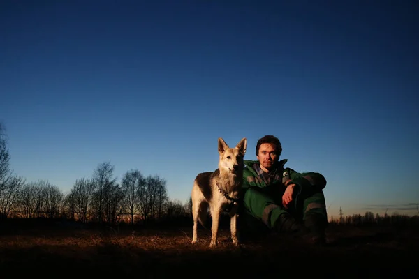 Homme avec chien à pied sur le champ th au coucher du soleil — Photo