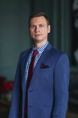 Uzun boylu, mavi takım elbiseli, kırmızı kravatlı, iç çamaşırı giymiş.