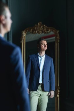 Yakışıklıymış. Mavi ceketli ve bej pantolonlu yakışıklı adam. Aynanın karşısında dikilip yan bakıyor.