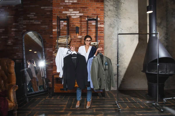 Glimlachende Jonge Vrouw Die Meerdere Hangers Met Mannenkleding Vasthoudt Moderne — Stockfoto