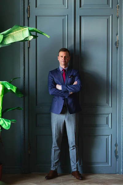 Tall man in blue suit and red tie posing in intertior studo