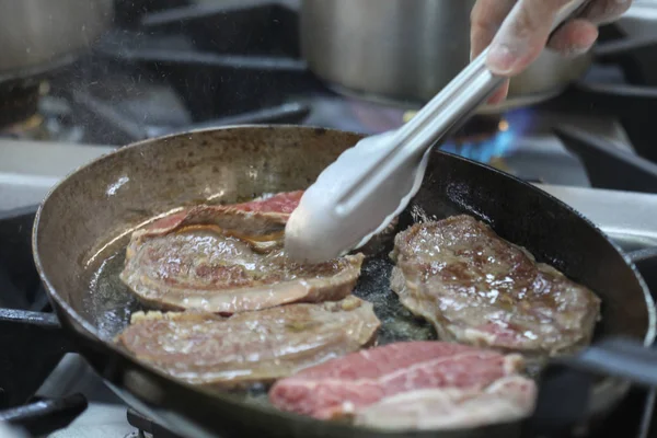 Şefin bulanık arka planı eti demir tavada kızartıyor. 