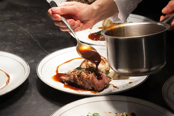Fundo embaçado do chef está derramando o molho na carne de vaca — Fotografia de Stock
