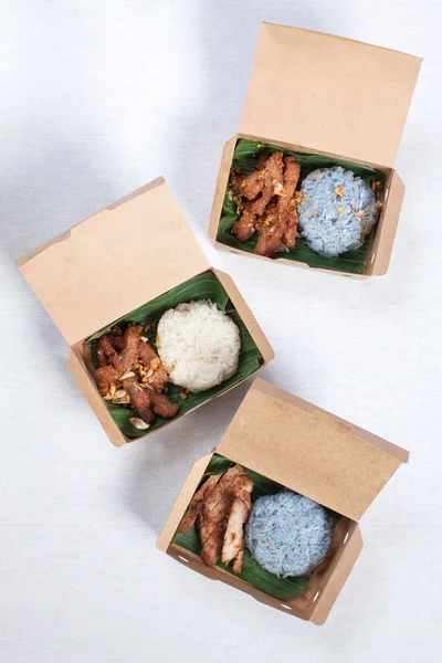 Izgara domuz eti ve kızarmış domuz etli yapış yapış pilav. Kahverengi bir karton kutuya konur.