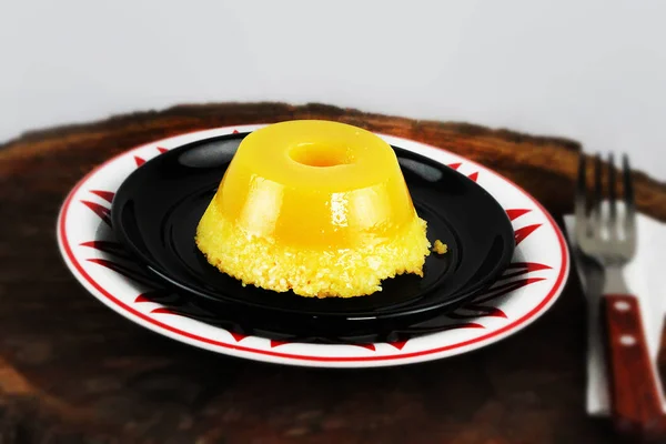 Brazilian sweet called Quindim that has as ingredients egg yolk, sugar and grated coconut, created in the southern Brazilian region. Quim on black dish and raw wood background