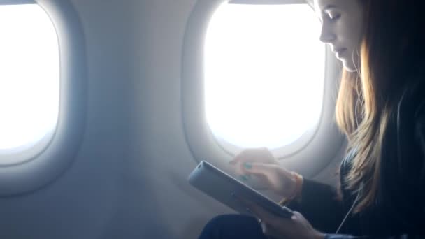 Woman is sitting and listening music at aircraft through tablet with headphones. — Stock Video