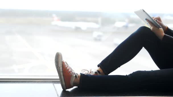 Mujer joven sosteniendo la tableta en las manos y sentado en el aeropuerto — Vídeo de stock