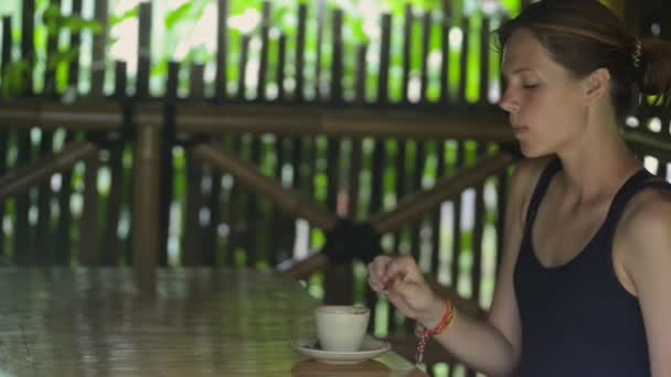 Mujer joven bebiendo café y comiendo en la mesa en la terraza en la isla de Bali . — Vídeos de Stock