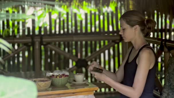 Lycklig amerikansk kvinna fotograferar mat och tar Selfie sitter på terrassen i Bali. — Stockvideo