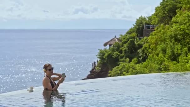 Mujer de negocios estadounidense que tiene videollamada con teléfono inteligente en la piscina en Asia resort . — Vídeos de Stock