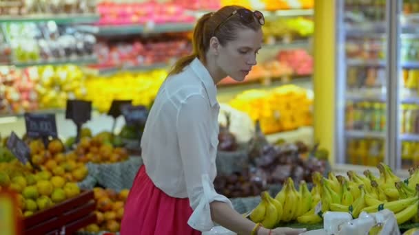 Молодая американка-покупатель выбирает банан, стоящий в продуктовом магазине . — стоковое видео