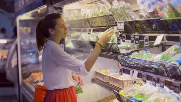 Genç vejetaryen kadın kokusu ve organik dükkanda ayakta yeşil sebzeler seçin. — Stok video