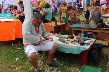 Shushenskoye, Russia - July 14, 2018: Man crafting a wooden spoon on master-class of annual International Festival of Music and Crafts World of Siberia (FestMirSibiri). An old Russian Slavic craft. clipart