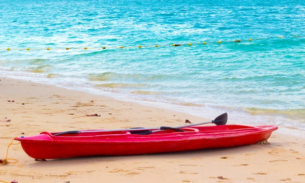 Empty red kayak boat on the sandy seashore with clear transparent turquoise water. Popular outdoor activity for tourists in sea travel on tropical seashore. Red boat marine of coast guardian.
