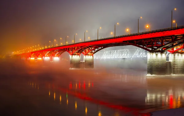 Night view on road bridge and railway bridge through the Yenisei River in Russia, Krasnoyarsk. Urban winter landscape. Light reflection on water surface. A long time of exhibiting.
