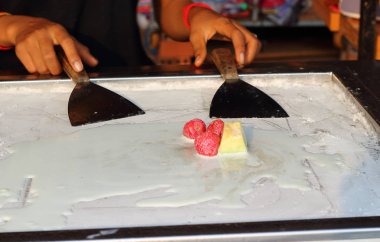 Strawberries, melons and milk for making rolls of stir fried ice cream in a freezing pan with spatulas. Popular dessert in Asia