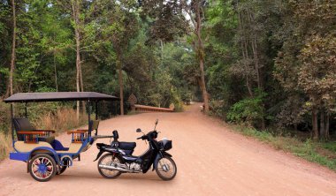 Geleneksel Tuk tuk taksi antik Angkor Wat, Kamboçya yoğun yağmur ormanı boyunca uzanan kırmızı tozlu yolda boş. Reklam kopya alanı ile egzotik seyahat için arka plan.