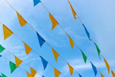 Arka planda mavi gökyüzüne karşı üçgen bayraklı çok renkli çelenkler