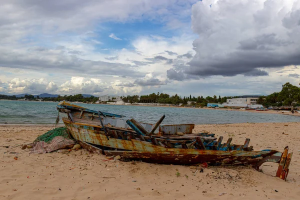 Old desolate fishing boat full of trash moored on sandy beach in Hammamet, Tunisia. Wreckage of a wooden boat on the seashore. Unnecessary trash polluting sea and coastal areas. Ecological background