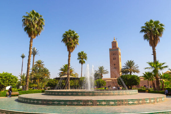 Marrakesh, Morocco - 12 October, 2019: Sunny view of Koutoubia Mosque from the city park Lalla Hasna with fountains and palm trees