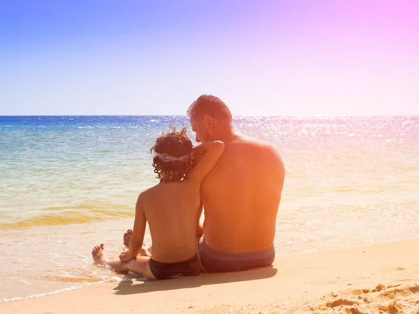 Padre e hijo se divierten en la playa tropical de arena blanca. Vista trasera del padre y el hijo sentados en la arena mirándose el uno al otro — Foto de Stock