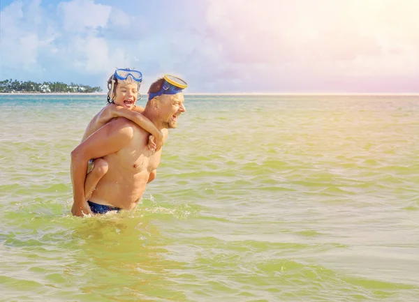 Het portret van vader bedrijf zoon op zijn schouders tijdens het zwemmen in de zee bij de kust. Vader geven zoon piggyback rit buiten glimlachen — Stockfoto