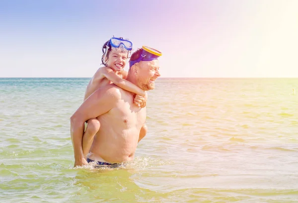 El retrato del padre sosteniendo al hijo sobre sus hombros mientras se baña en el mar en la costa. Padre dando hijo paseo a cuestas al aire libre sonriendo — Foto de Stock