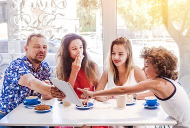 Kahvaltı ve tablet kullanarak mutlu bir aile. Mutlu bir adam ve internet, kullanarak seyir perde için üç çocukları gülümseyen kafe, dijital tablet olan büyük bir şirket online satın