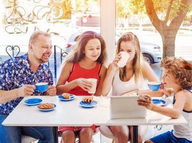 Kahvaltı ve tablet kullanarak mutlu bir aile. Mutlu bir adam ve internet, kullanarak seyir perde için üç çocukları gülümseyen kafe, dijital tablet olan büyük bir şirket online satın