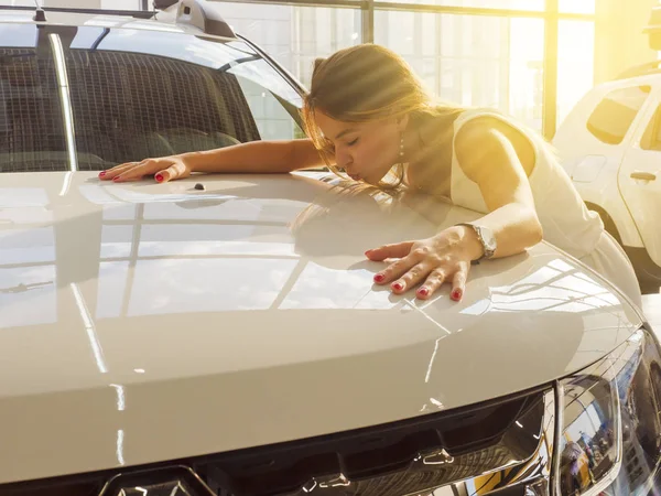 Dream about car. Gorgeous smiling woman kissing hood of new white car in the dealership.