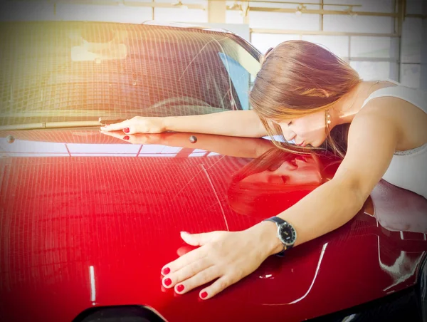 Dream about car. Gorgeous smiling woman kissing hood of new red car in the dealership.