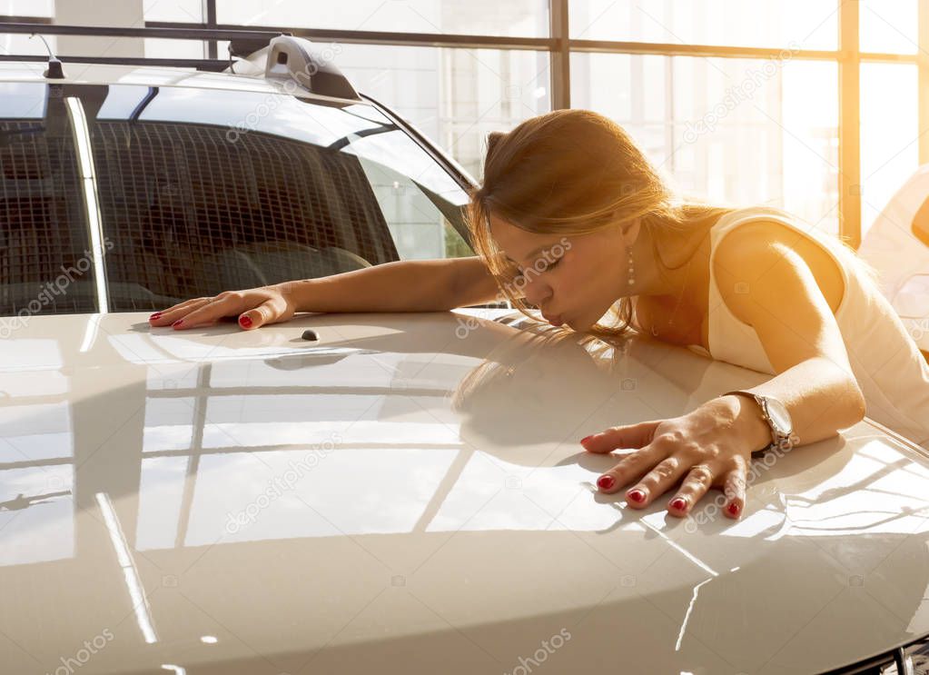 Dream about car. Gorgeous smiling woman kissing hood of new white car in the dealership.