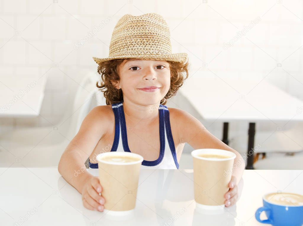 A child standing by the bar counter of a cafe and taking two cups of coffee