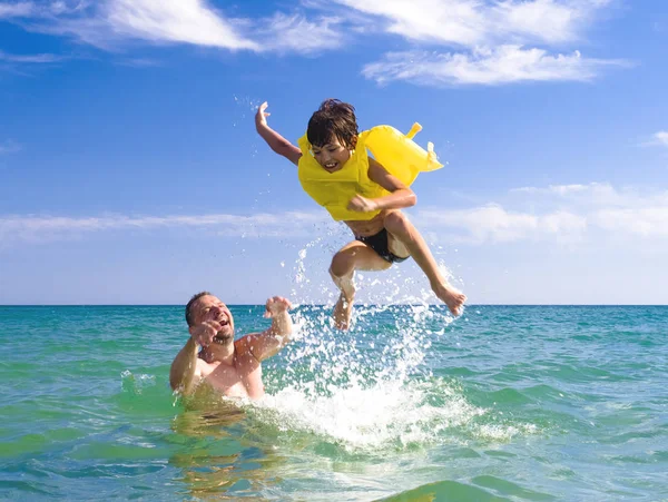 Dad throws up his son in an inflatable life jacket in the sea.Safety Concerns Concept