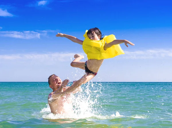 Vader Gooit Zijn Zoon Een Opblaasbare Reddingsvest Zee Bezorgdheid Veiligheidsconcept — Stockfoto