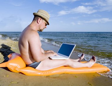 Deniz kenarında güzel yeri dizüstü bilgisayar kullanan adam