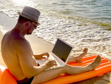 Deniz kenarında güzel yeri dizüstü bilgisayar kullanan adam