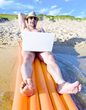 Sahilde dinlenirken dizüstü bilgisayarda çalışan adam. İşadamı bir şişme şişme kumlu bir plaj üzerinde bir dizüstü bilgisayar ile