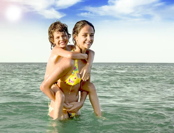 The portrait of an older sister holding her little brother on her shoulders while bathing in the sea at the coast. Sister giving brother a piggyback ride outdoors smiling