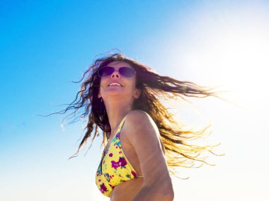 Güzel romantik kız açık havada. Güzel Model parlak güneşin arka planda bir tropik sahil üzerinde sarı bir mayo içinde. Uzun saçları rüzgarda. Arkadan aydınlatmalı, sıcak renk tonları