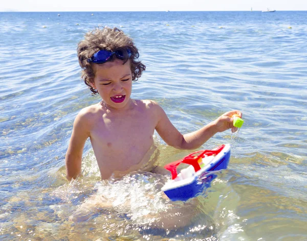 Bambino che gioca con il giocattolo della nave in mare. Bambino os in vacanza in estate in spiaggia in vacanza — Foto Stock