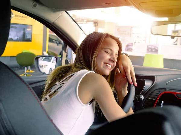 Genç ve güzel bir kadın araba dümeninde yatıyor, gözlerini kapıyor ve sarılıyor. Araç satın aldıktan sonra araba galerisinin mutlu müşterisi.