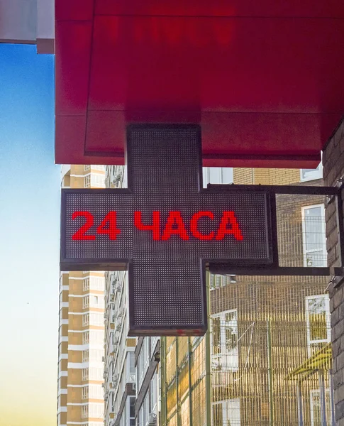 pharmacy signboard on the building - red to 24 hours on the background of the dark cross