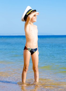 Mavi deniz ve gökyüzü arka plan üzerinde mesafe bakarak bir deniz şapkalı siyah yüzme şort komik çocuk