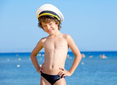 Mavi deniz ve gökyüzü arka plan üzerinde kameraya bakarak bir deniz şapkalı komik çocuk