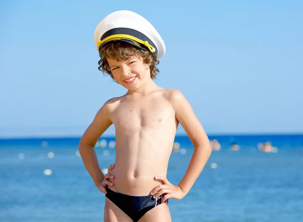 Mavi deniz ve gökyüzü arka plan üzerinde kameraya bakarak bir deniz şapkalı komik çocuk